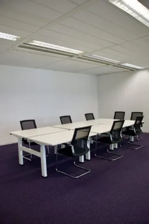 Vergaderruimte met acht zwarte stoelen en witte tafels op een paarse tapijtvloer in een kantoorgebouw aan het Koningin Wilhelminaplein.