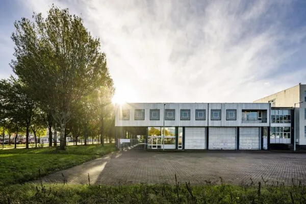 Wit bedrijfsgebouw aan de Van der Madeweg met meerdere garagedeuren en bomen in de ochtendzon.