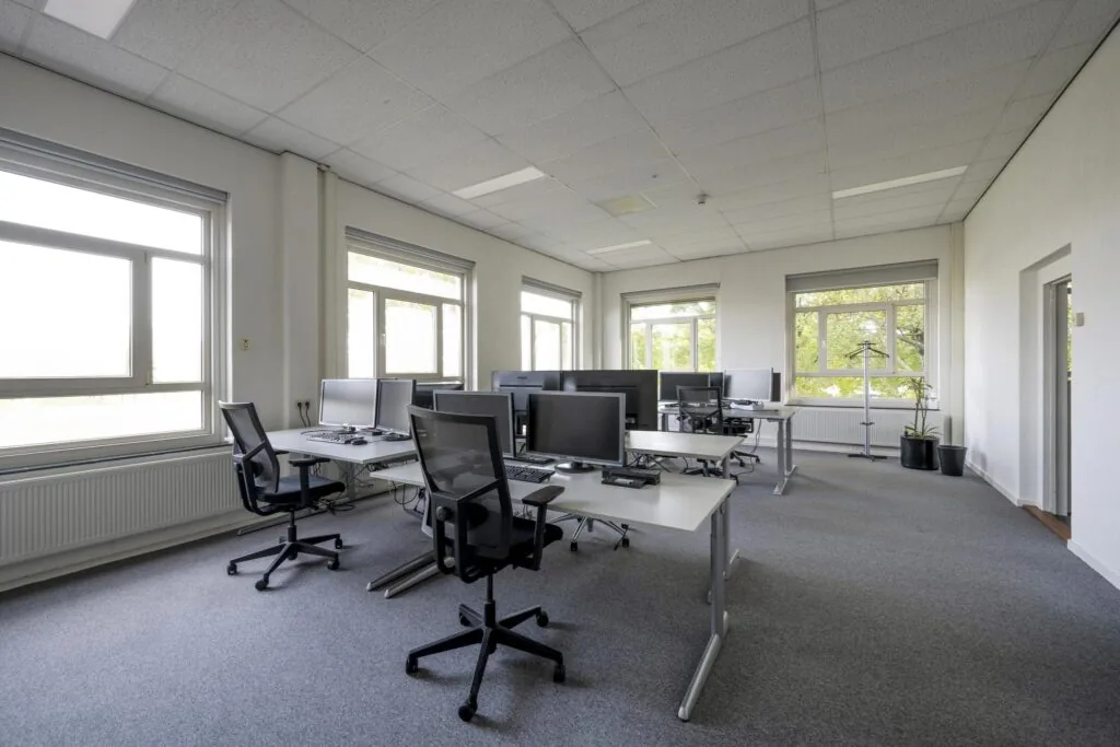 Modern en licht kantoorinterieur aan de Van der Madeweg met meerdere bureaus, computerschermen en ergonomische bureaustoelen.