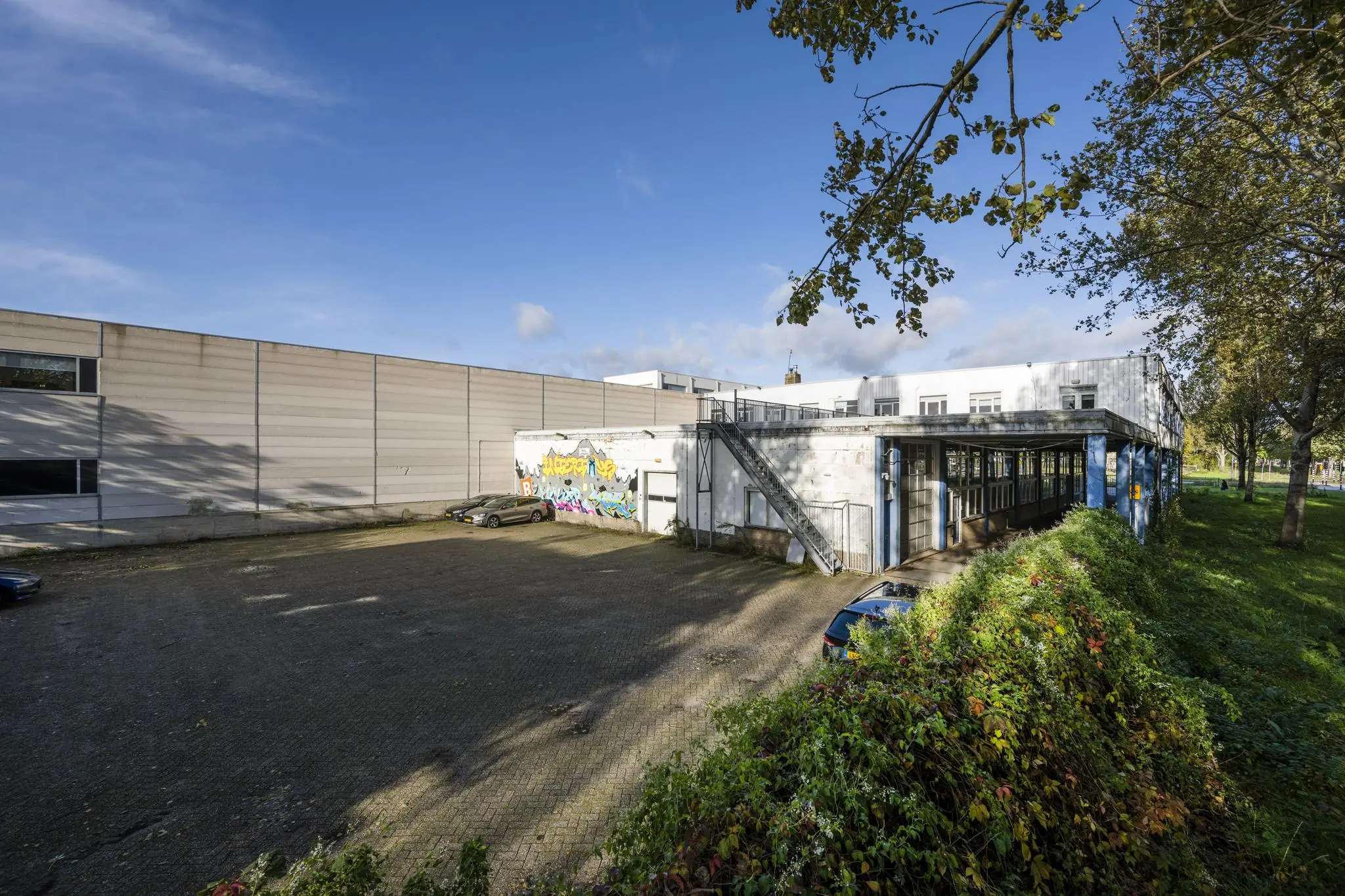 Bedrijventerrein aan de Van der Madeweg met een wit gebouw, graffiti op de muur en geparkeerde auto's op een zonnige dag.