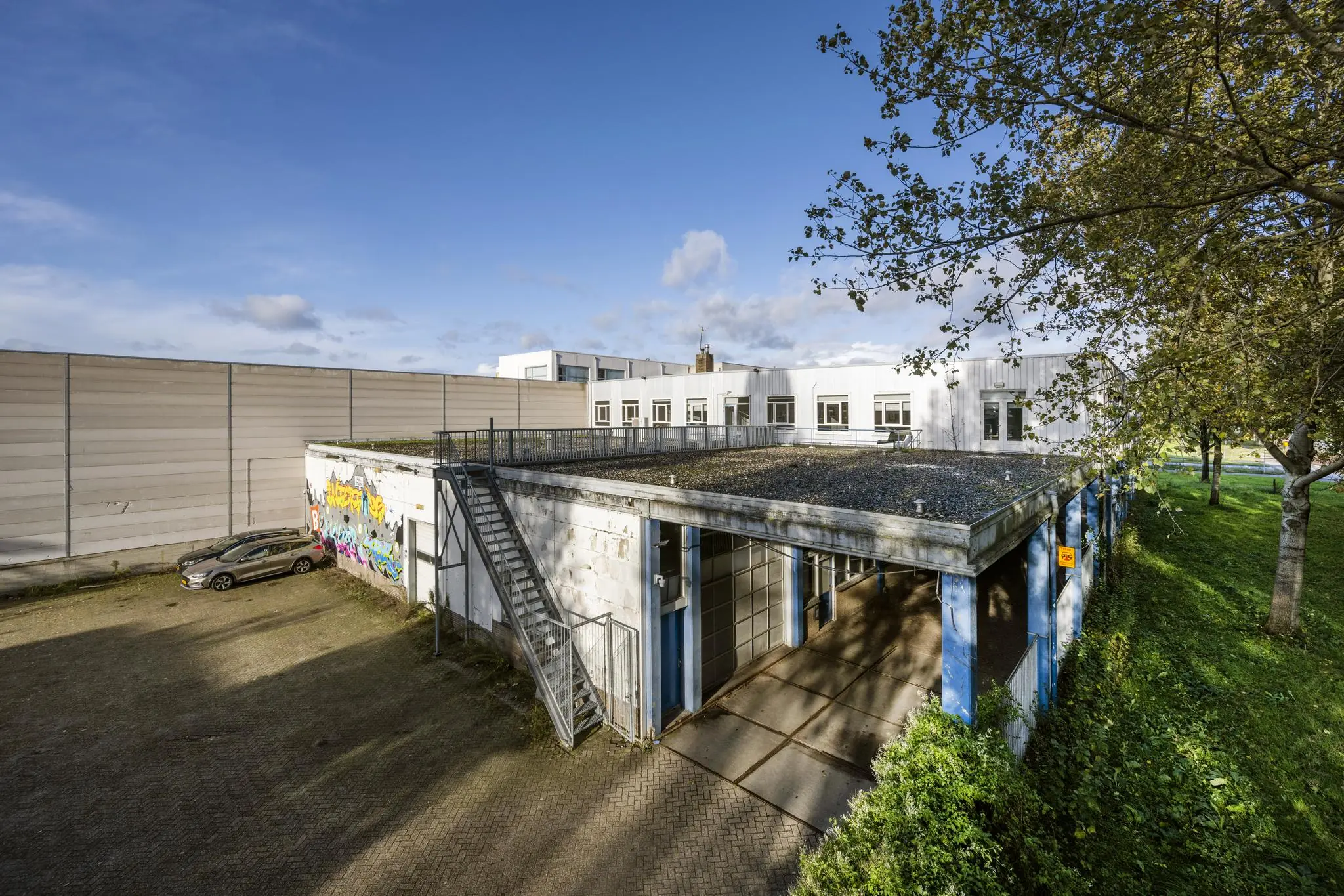Wit bedrijfsgebouw aan de Van der Madeweg met graffiti, blauwe kolommen en aangrenzend parkeerterrein.