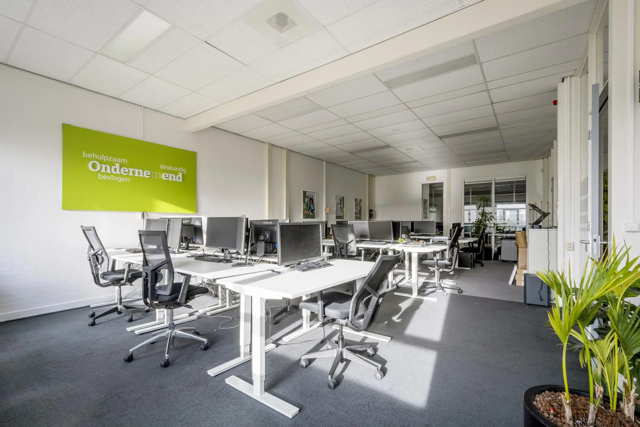 Licht en modern kantoorinterieur aan de Van der Madeweg met meerdere werkplekken, bureaustoelen en een groene inspiratiewand.