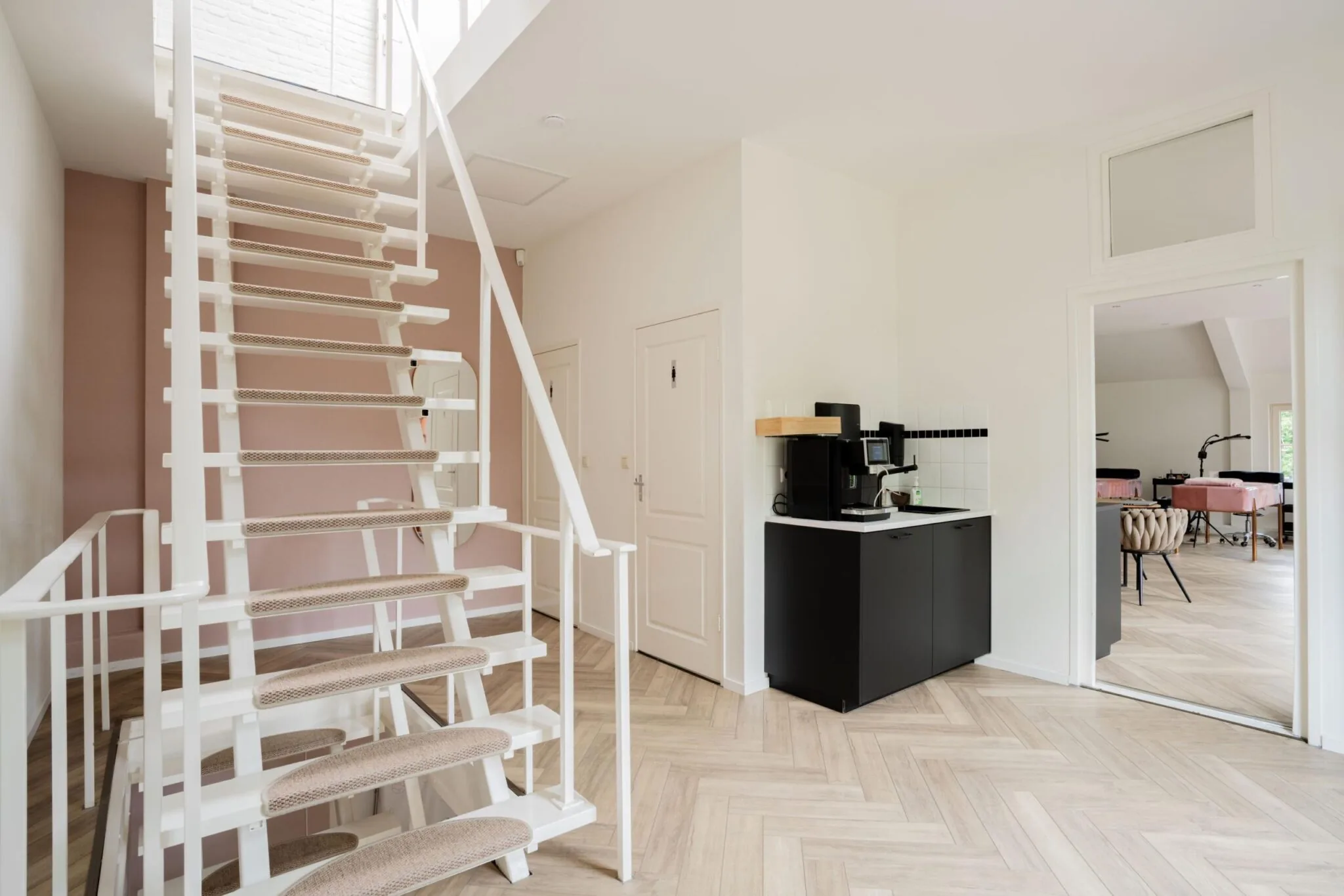 Moderne hal met witte open trap, koffiecorner en zicht op een lichte ruimte met behandelstoelen aan de Sloterweg.