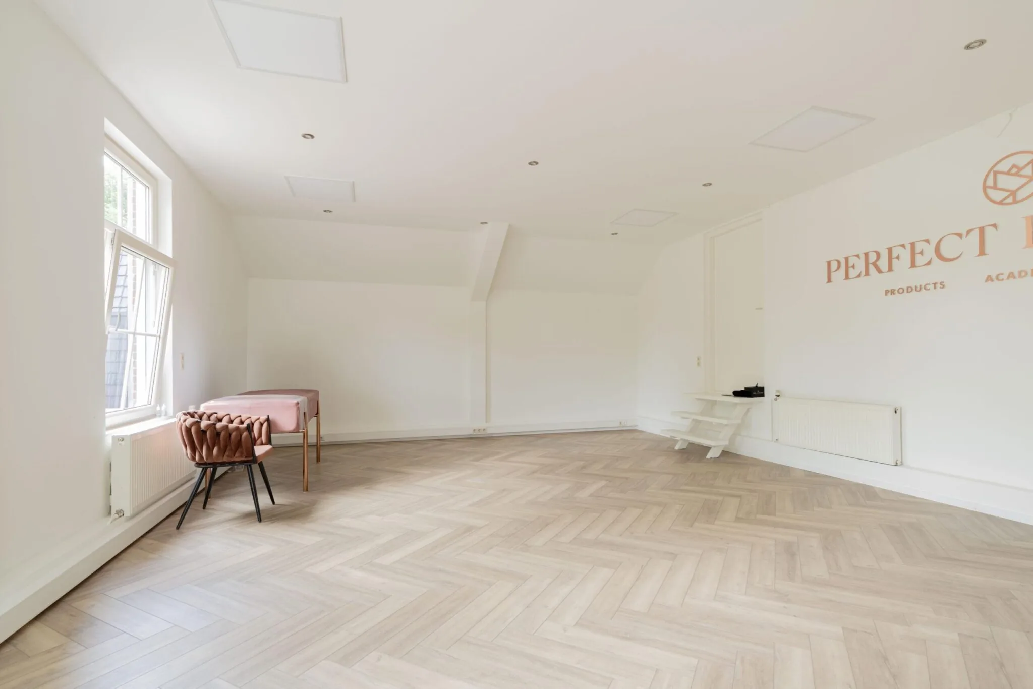Lichte, minimalistisch ingerichte ruimte aan de Sloterweg met visgraatvloer, behandelbed en roze accenten.