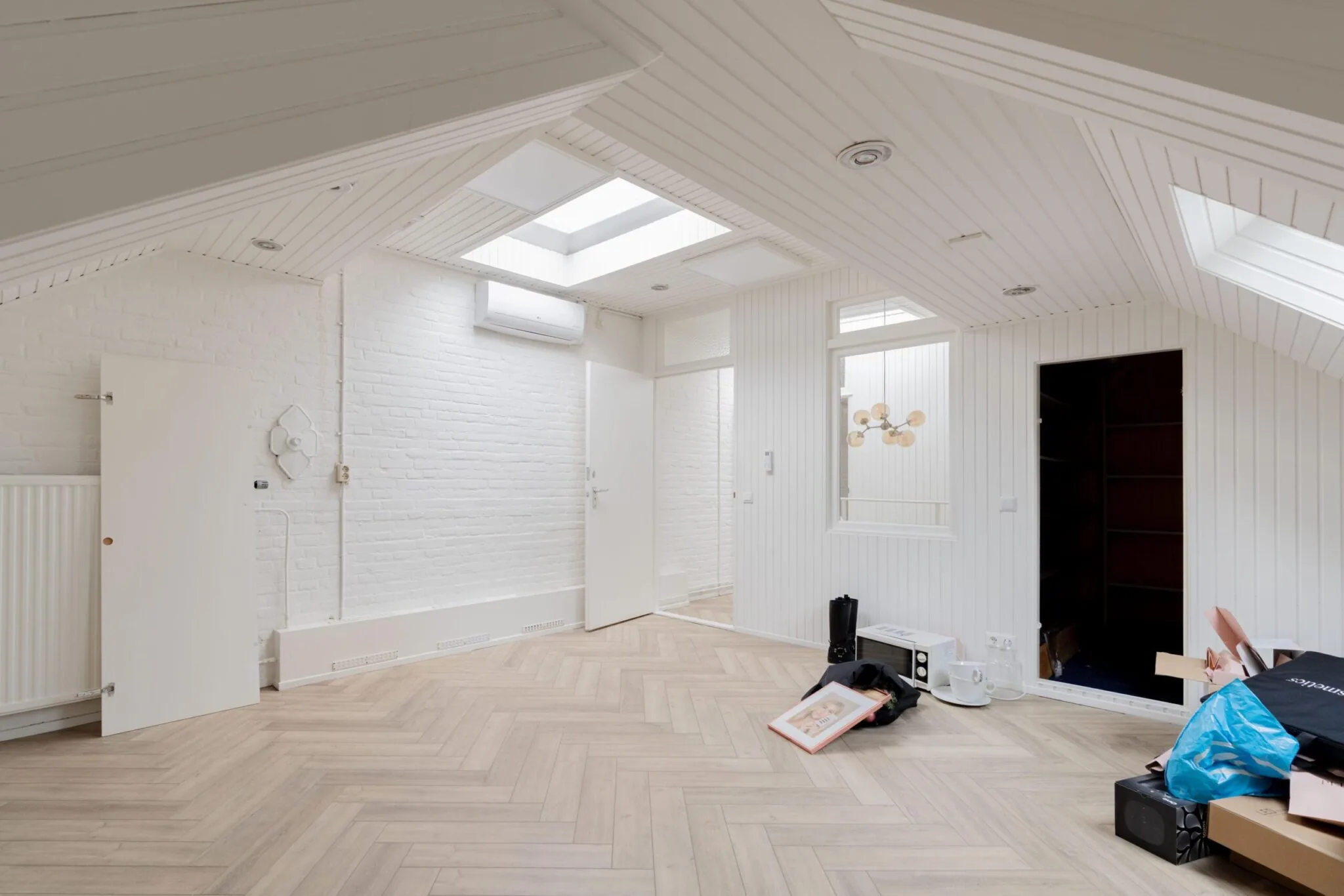 Zolderkamer aan de Sloterweg met witte houten wanden, dakramen, ingebouwde kast en licht houten visgraatvloer.