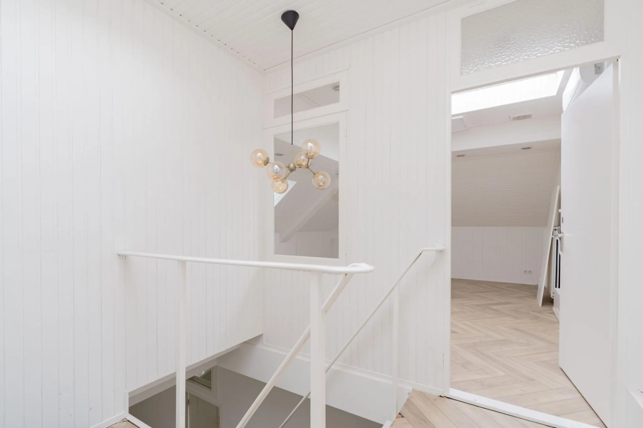 Witgeschilderde overloop met moderne hanglamp en toegang tot een zolderkamer aan de Sloterweg.