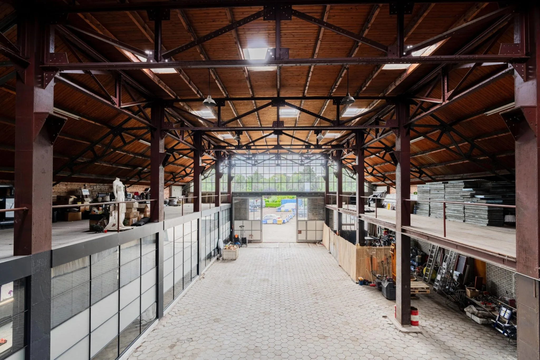Ruime industriële loods aan de Sloterweg met hoge houten kap, stalen constructie en bovenverdiepingen vol opslagmateriaal.