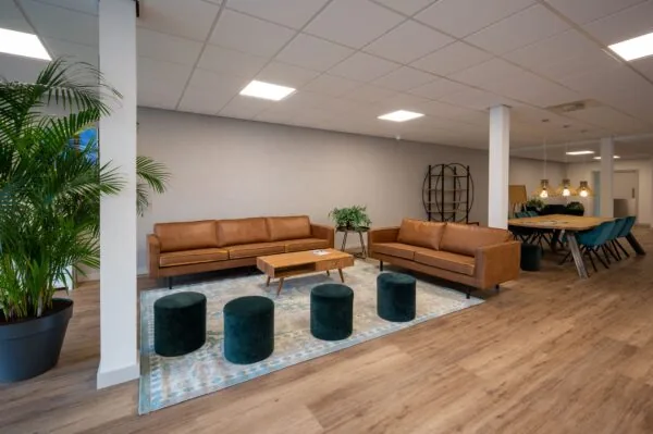 Modern ingerichte zithoek op Vlierberg met leren banken, fluwelen poefjes en houten meubels in een open ruimte.
