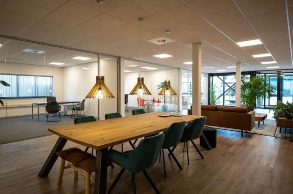 Modern kantoorinterieur aan de Vlierberg met glazen vergaderruimtes, houten vergadertafel en een loungehoek met planten.