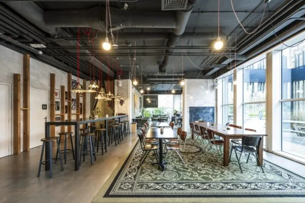 Moderne gemeenschappelijke werkruimte aan de Laan van Kronenburg met lange tafels, hoge krukken en grote ramen voor veel daglicht.
