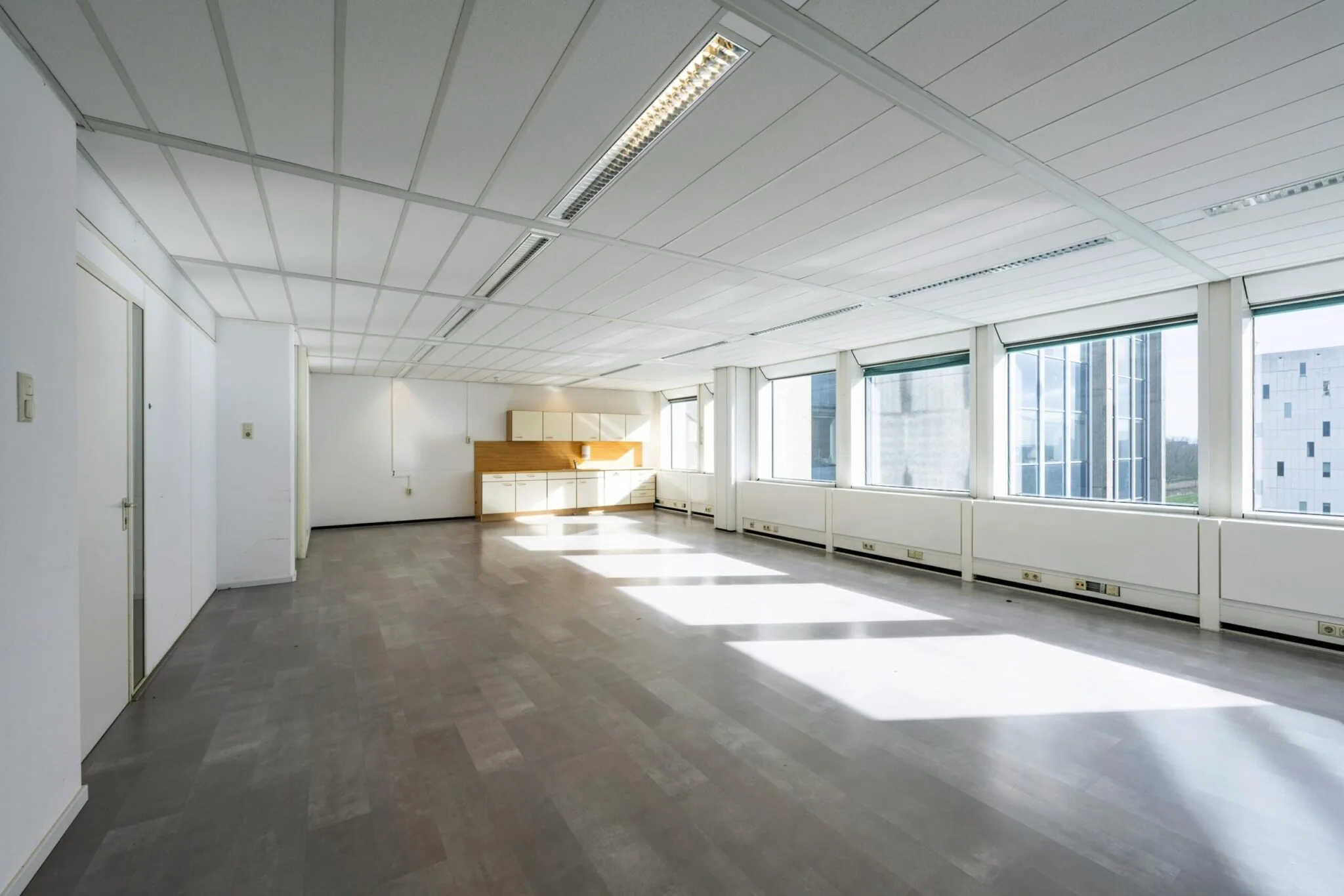 Licht en ruim leeg kantoorpand aan de Laan van Kronenburg met grote ramen en ingebouwde kitchenette.