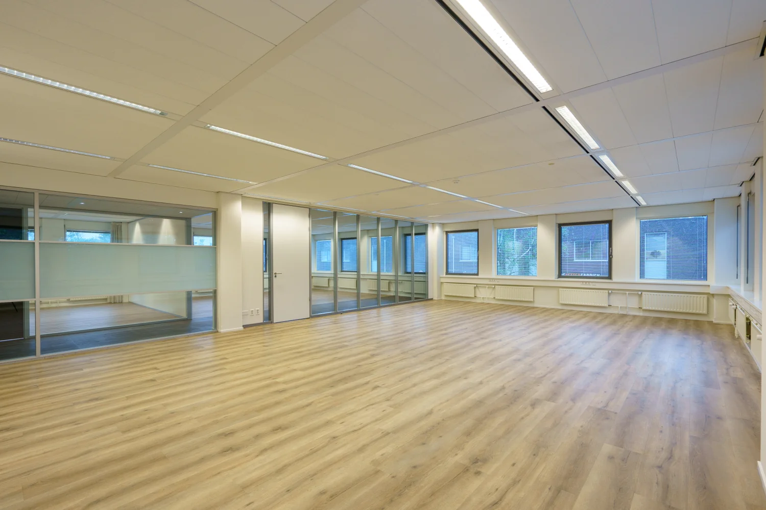 Licht en ruim kantoorpand aan de Baarnsche Dijk met houten vloer, glazen wanden en grote ramen.
