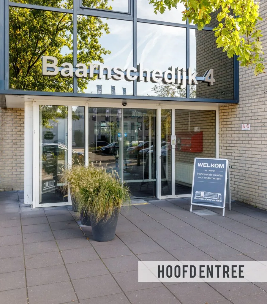 Hoofdentree van het gebouw aan de Baarnsche Dijk 4 met glazen deuren, plantenbakken en welkomstbord.