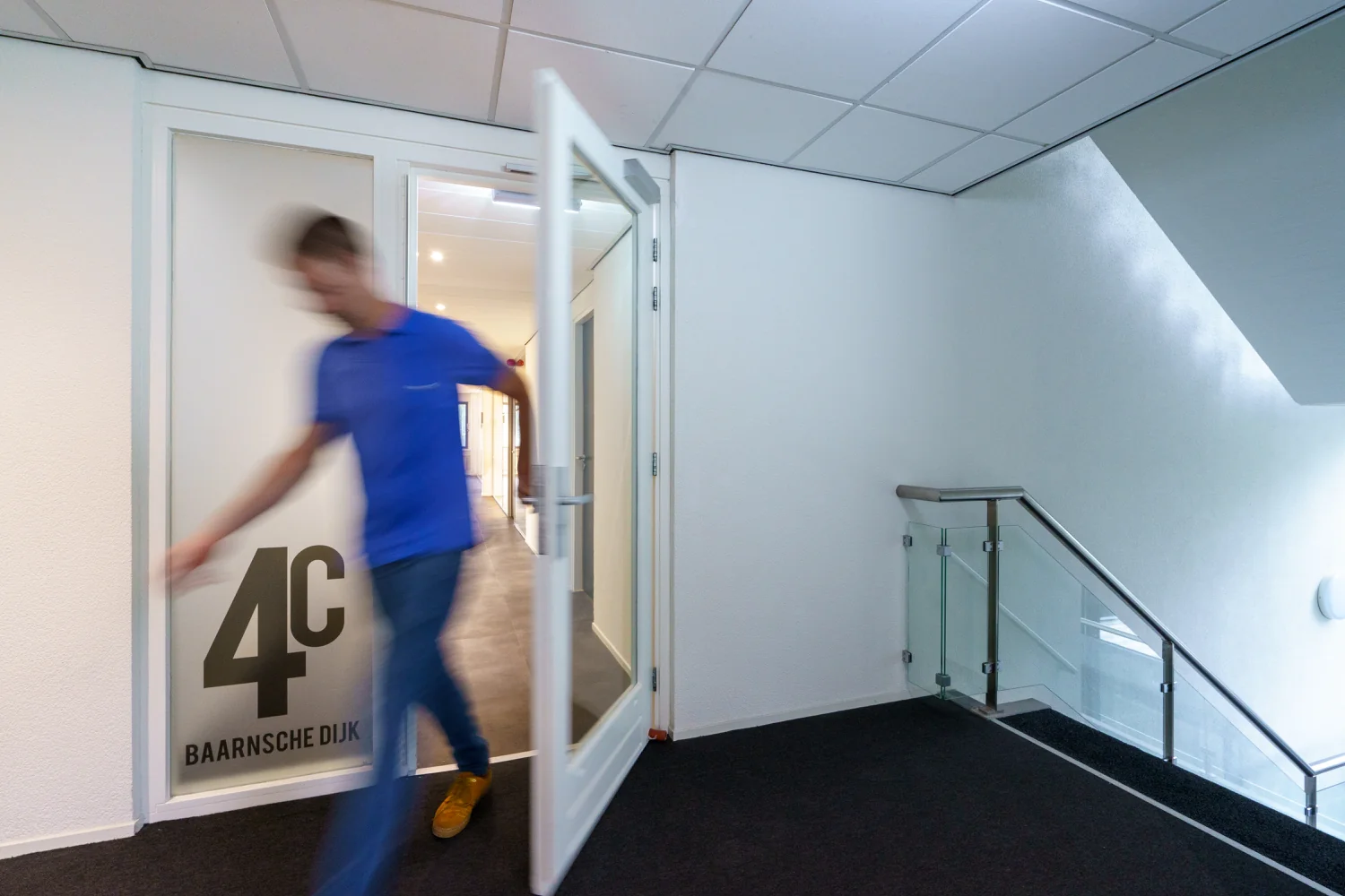 Man komt in beweging een kantoorruimte uit op de Baarnsche Dijk 4C via een openstaande deur bij een trapopgang.