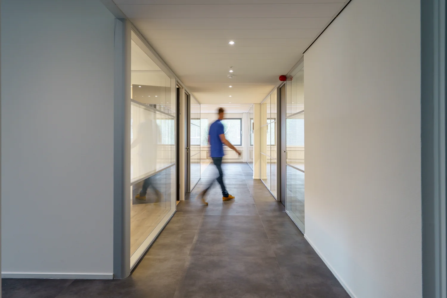 Een man loopt door een moderne gang met glazen kantoorkamers aan de Baarnsche Dijk.
