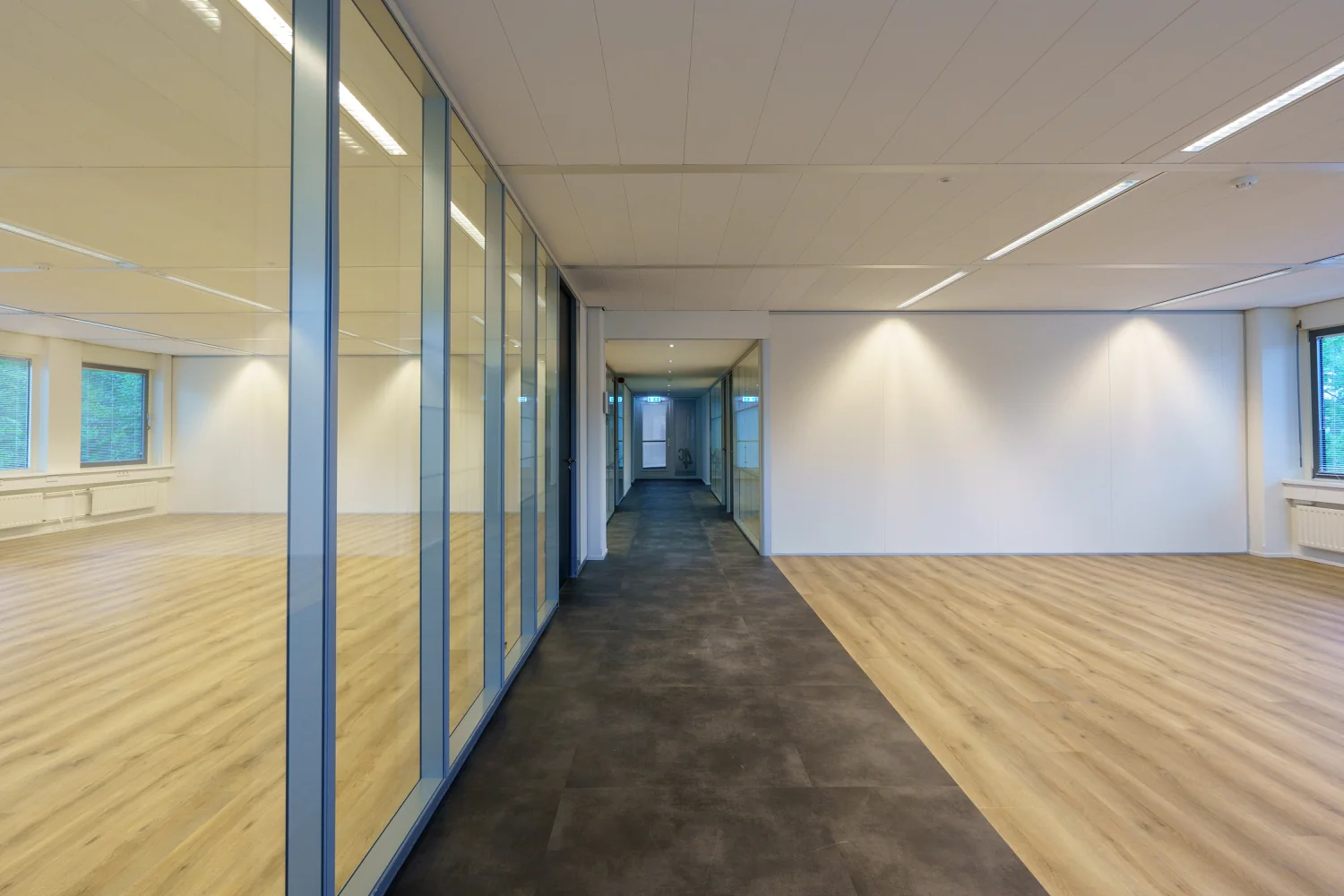 Moderne, lege kantoorruimte aan de Baarnsche Dijk met glazen wanden, licht houtkleurig laminaat en een donkere gangvloer.