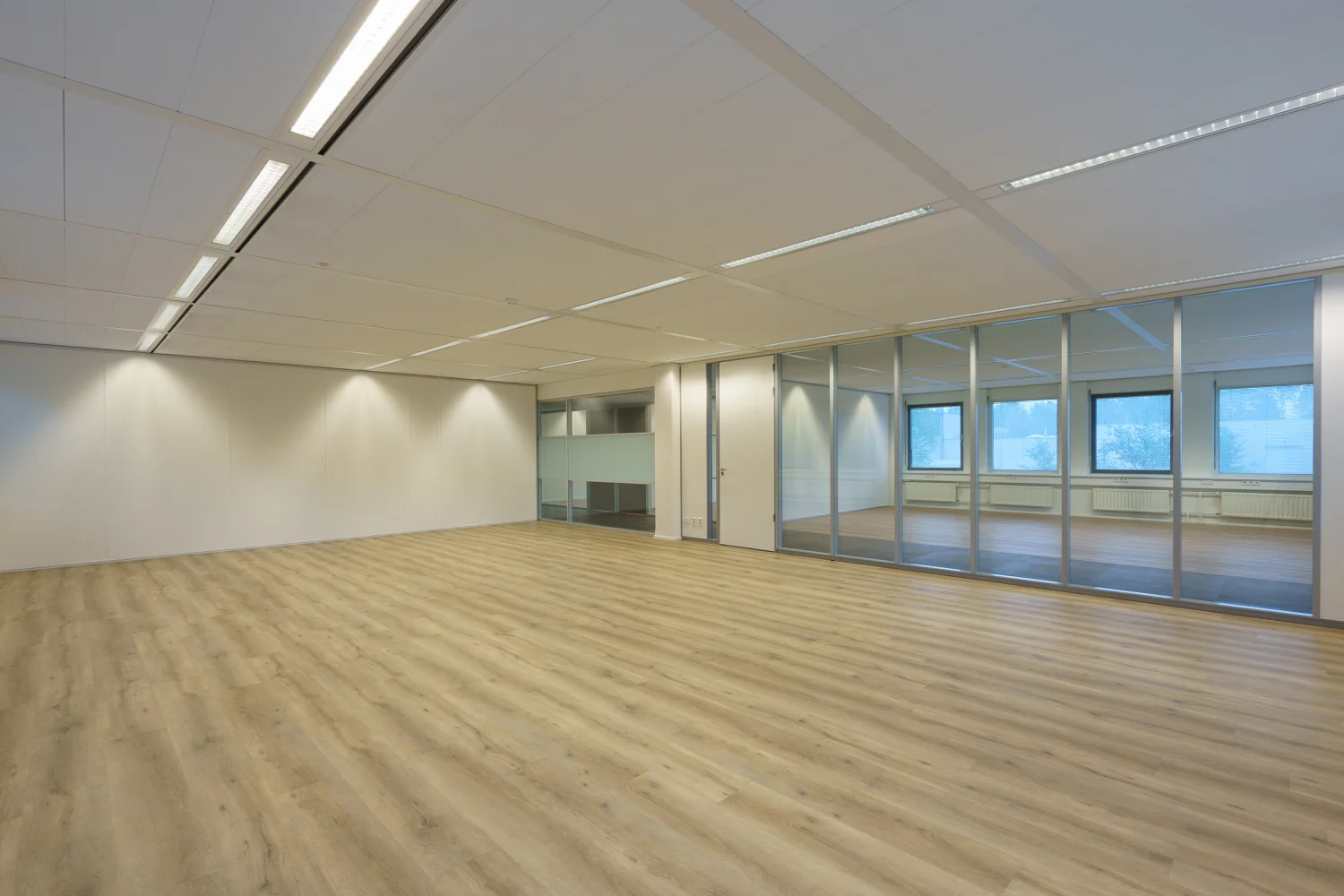 Leeg, modern kantoorinterieur aan de Baarnsche Dijk met houten vloer en glazen scheidingswand.