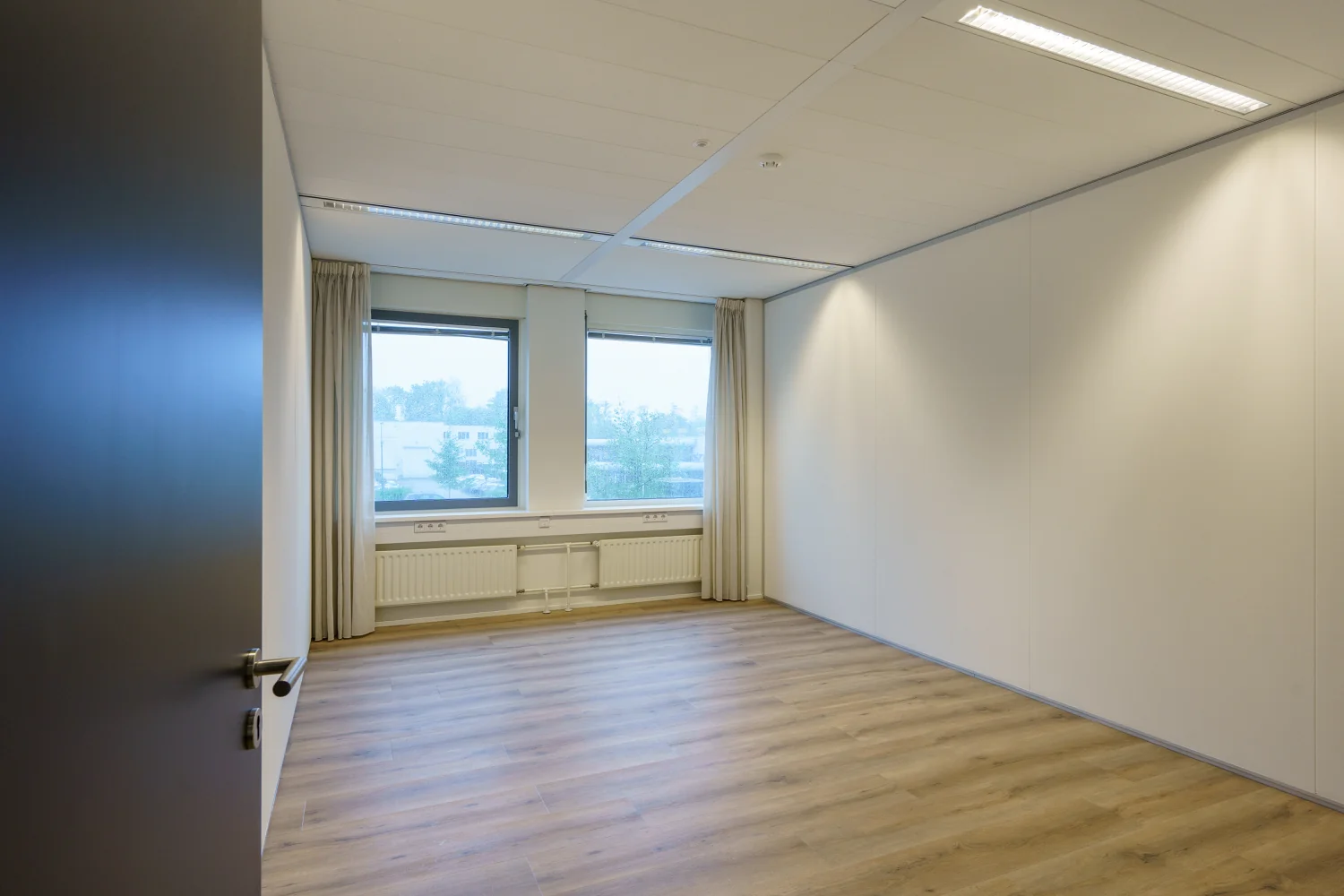 Leeg kantoor met houten vloer, witte muren en twee ramen aan de Baarnsche Dijk.
