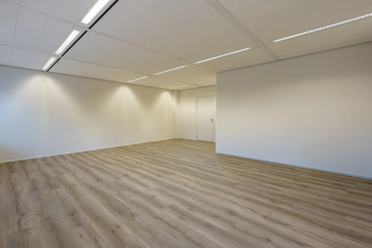 Leeg kantoorruimte met houten vloer, witte wanden en systeemplafond aan de Baarnsche Dijk.