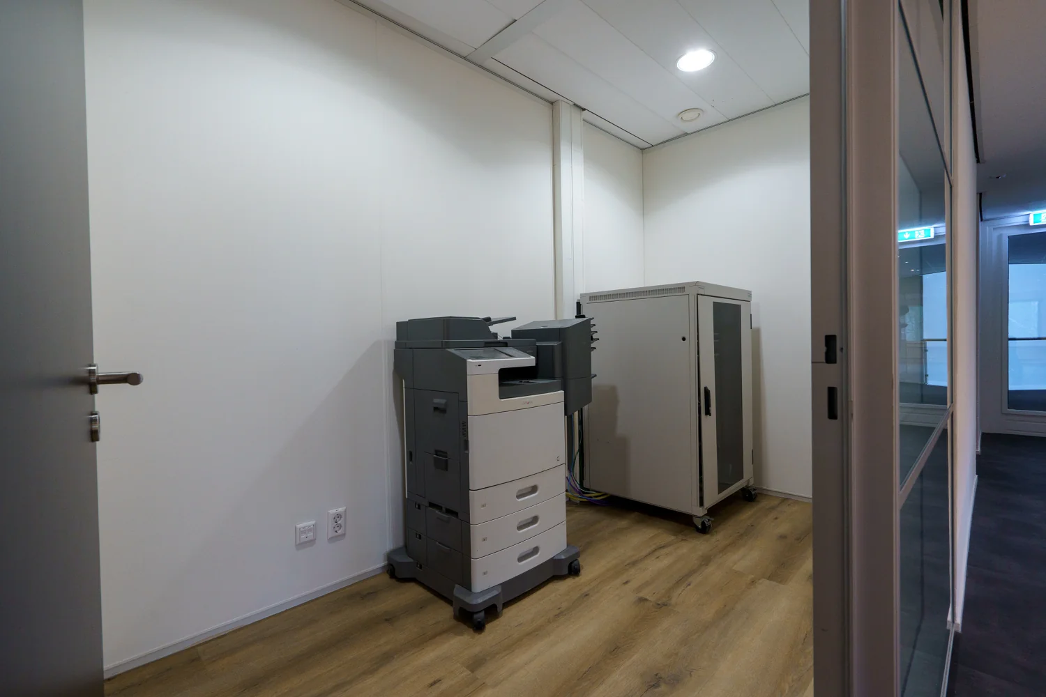 Kleine kantoorruimte aan de Baarnsche Dijk met een printer en een serverkast op een houten vloer.