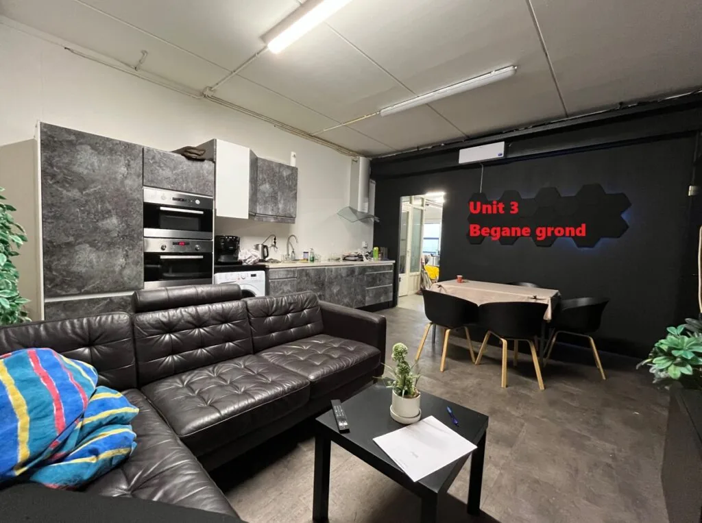 Moderne woonkamer en keuken in Unit 3 op de begane grond van Bergveste, met zwart leren bank, eettafel en keukenkastjes in betonlook.