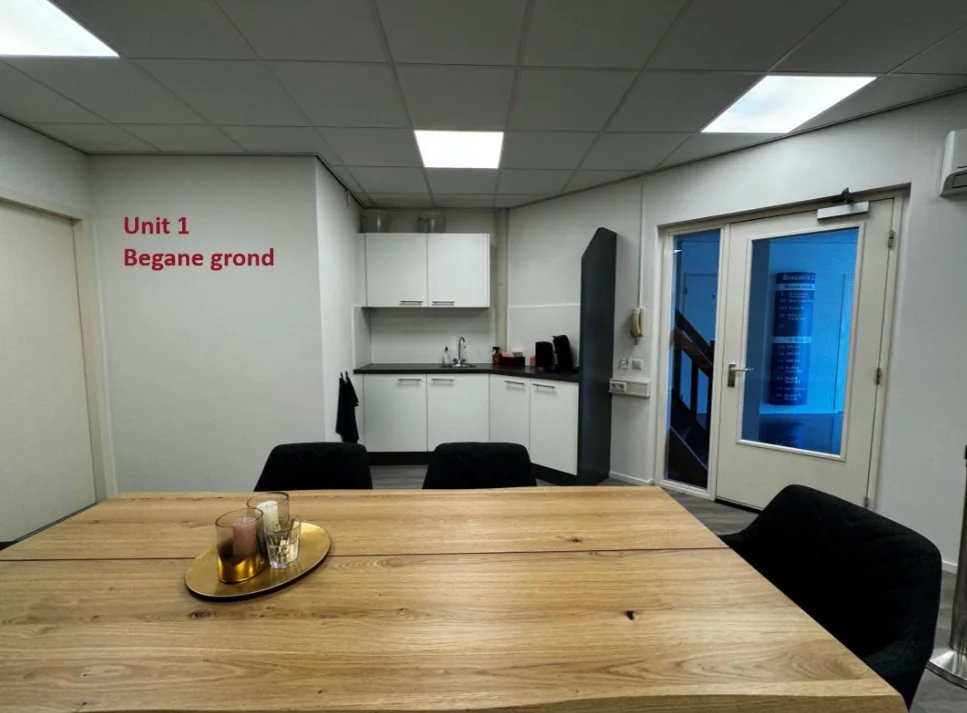 Kantoorruimte met een zithoek, kitchenette en de aanduiding "Unit 1 Begane grond" op de muur.