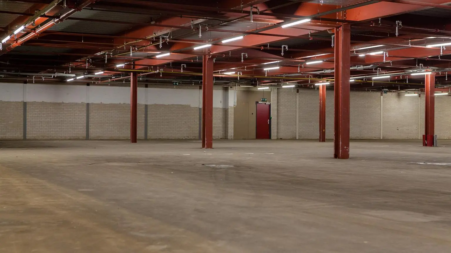 Lege industriële ruimte met betonnen vloer, rode stalen balken en bakstenen muren aan de Weesperstraat.