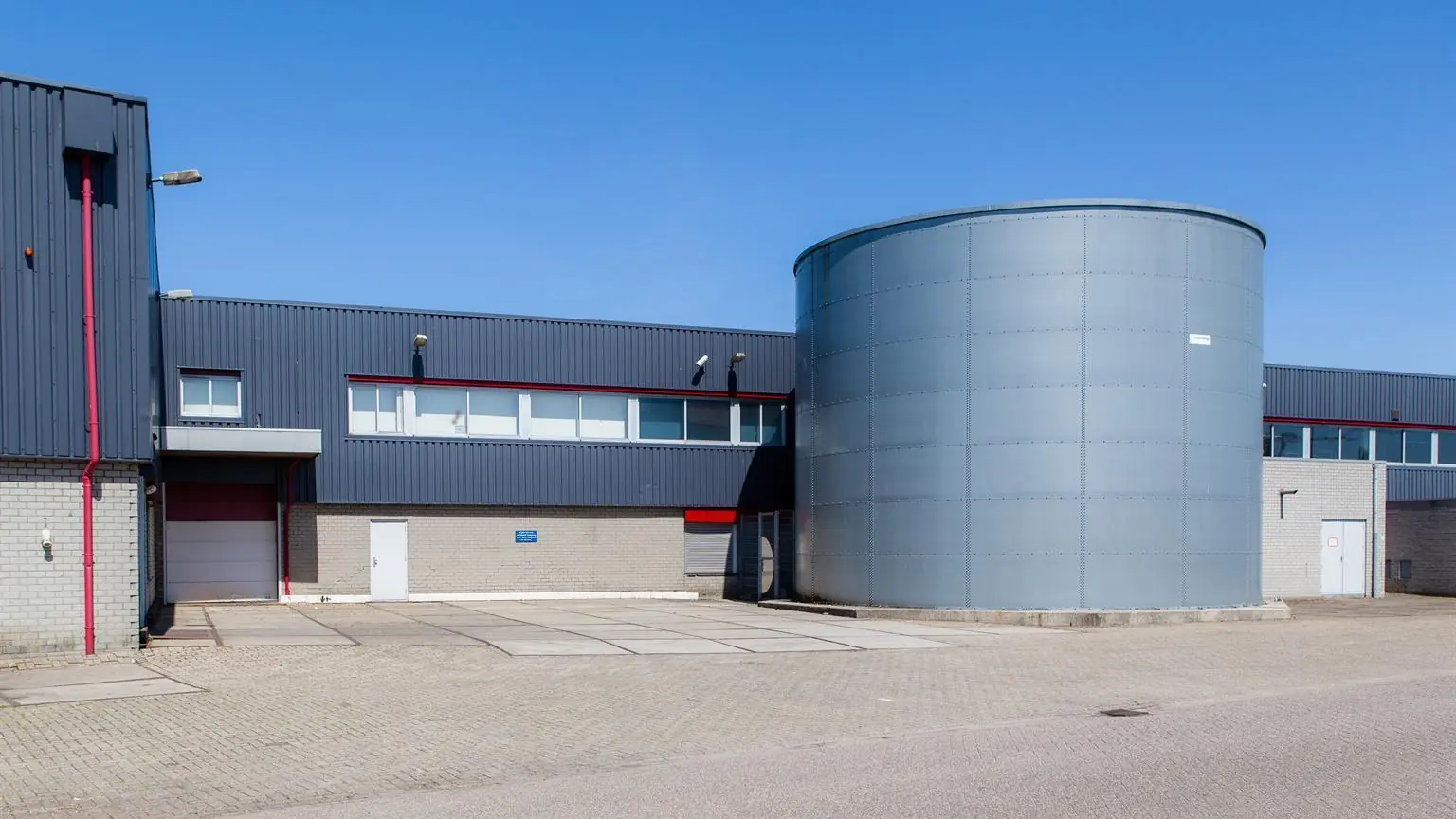 Bedrijventerrein met een modern industrieel gebouw en een grote ronde metalen silo aan de Weesperstraat.