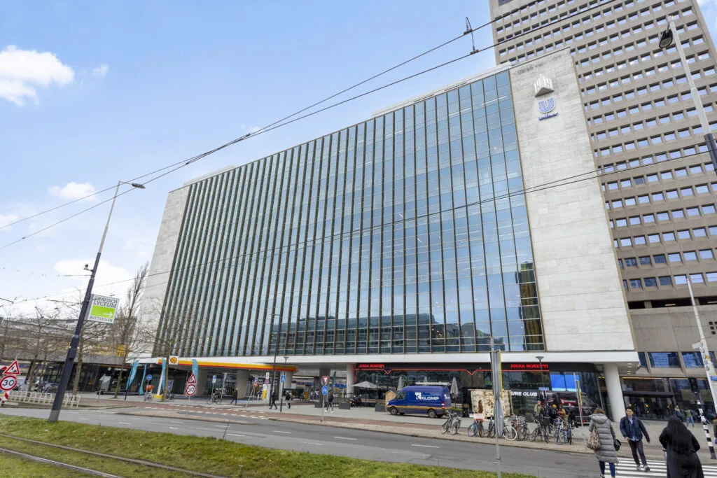 Een modern kantoorpand aan het Hofplein in Rotterdam, met een glazen façade en winkels op de begane grond.
