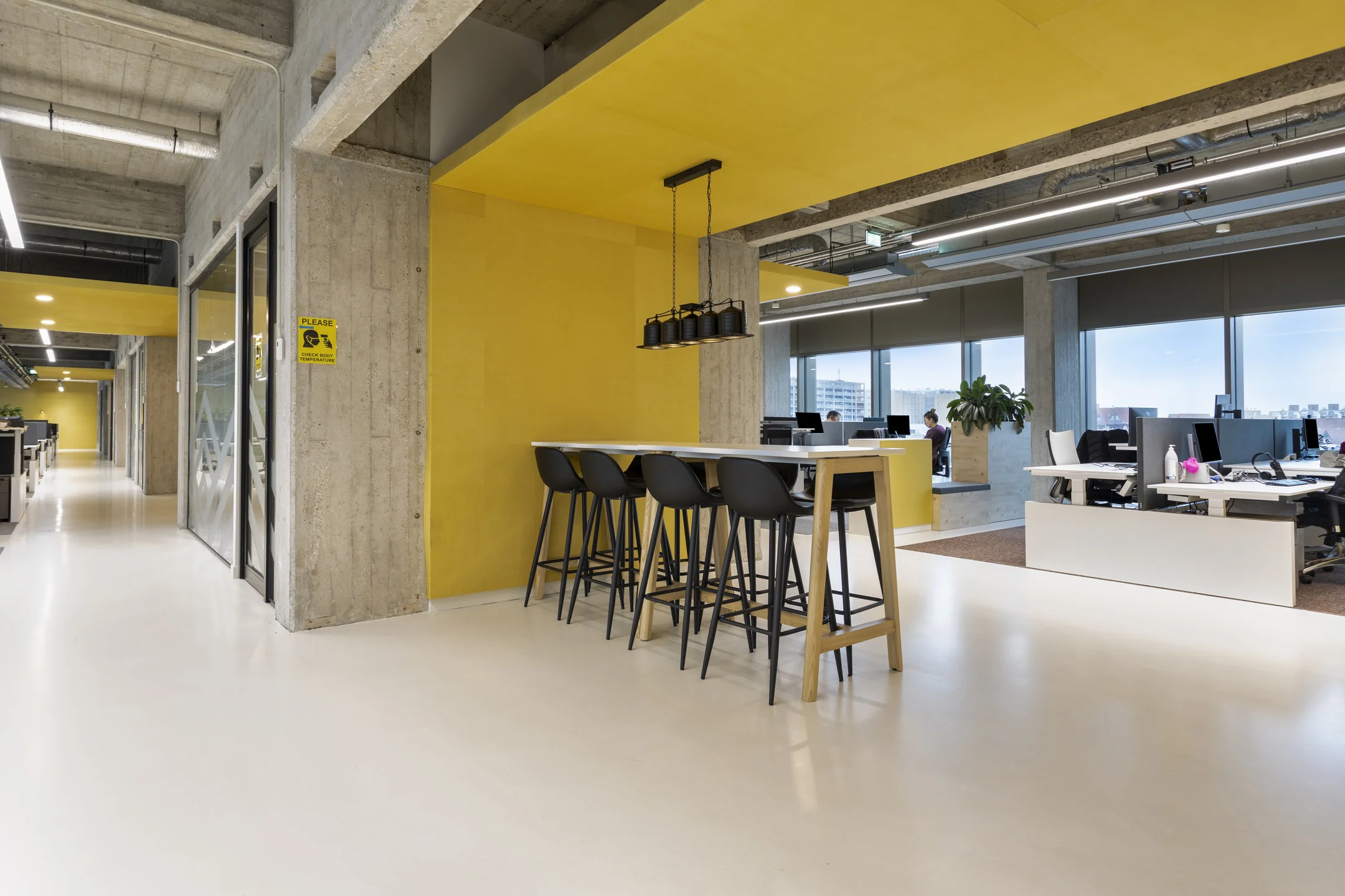 Een moderne kantoorruimte met gele accenten, hoge tafels en werkplekken.