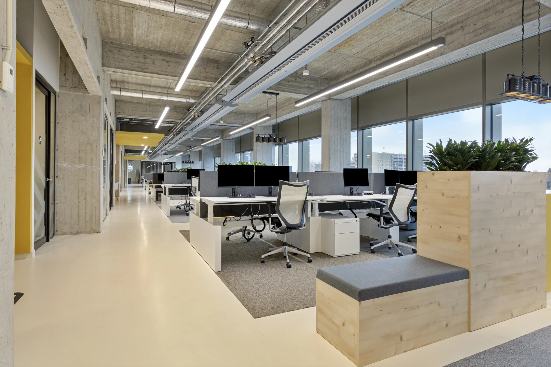 Een moderne, open kantoorruimte met bureaus, stoelen, en plantenbakken.