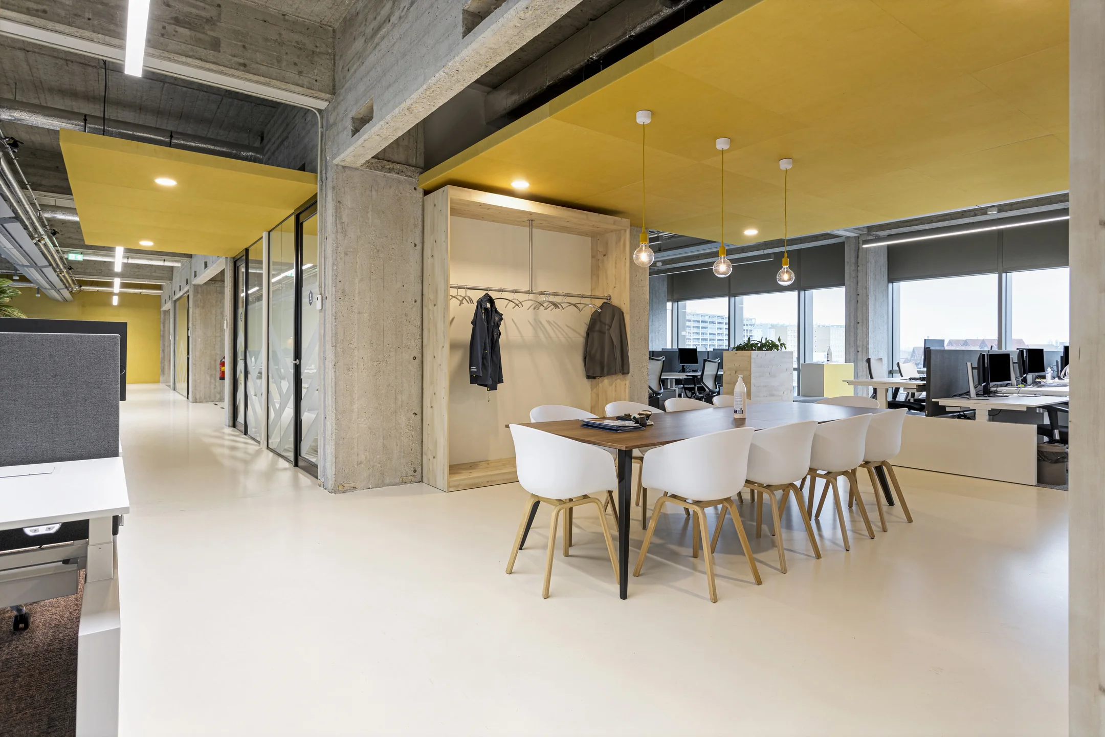Een moderne kantoorruimte met een vergadertafel, witte stoelen en gele plafonddetails.