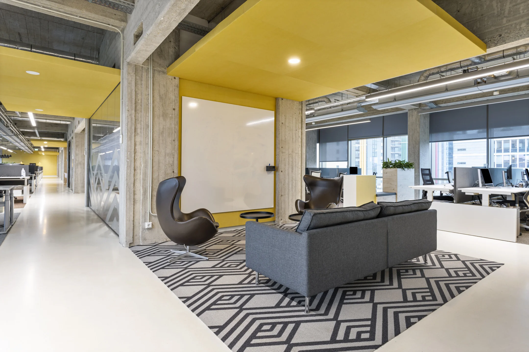 Moderne kantoorruimte met gele accenten, een witte schrijfwand, comfortabele stoelen en werkplekken met computers.