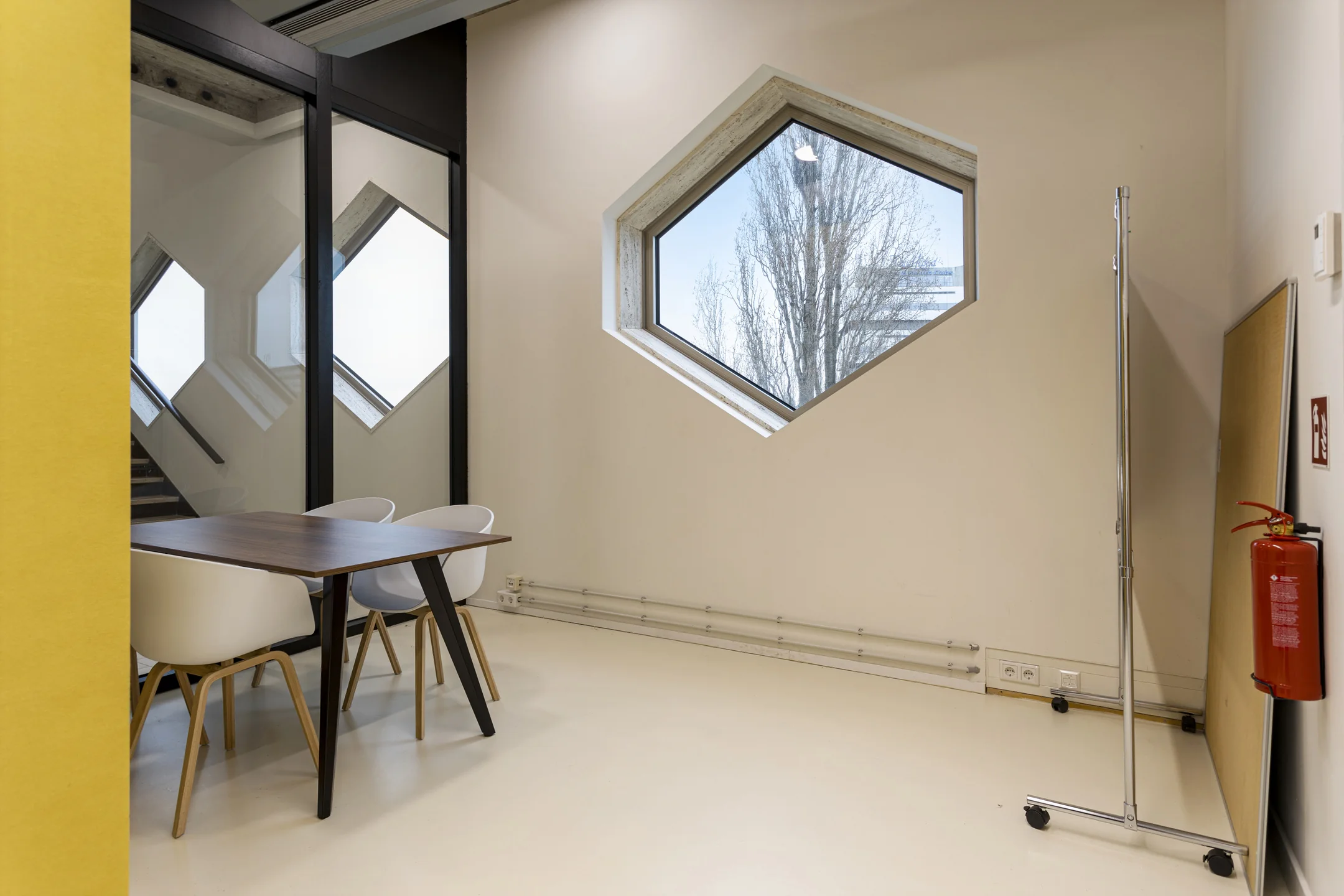 Een moderne vergaderruimte met zeshoekige ramen en een houten tafel met witte stoelen.