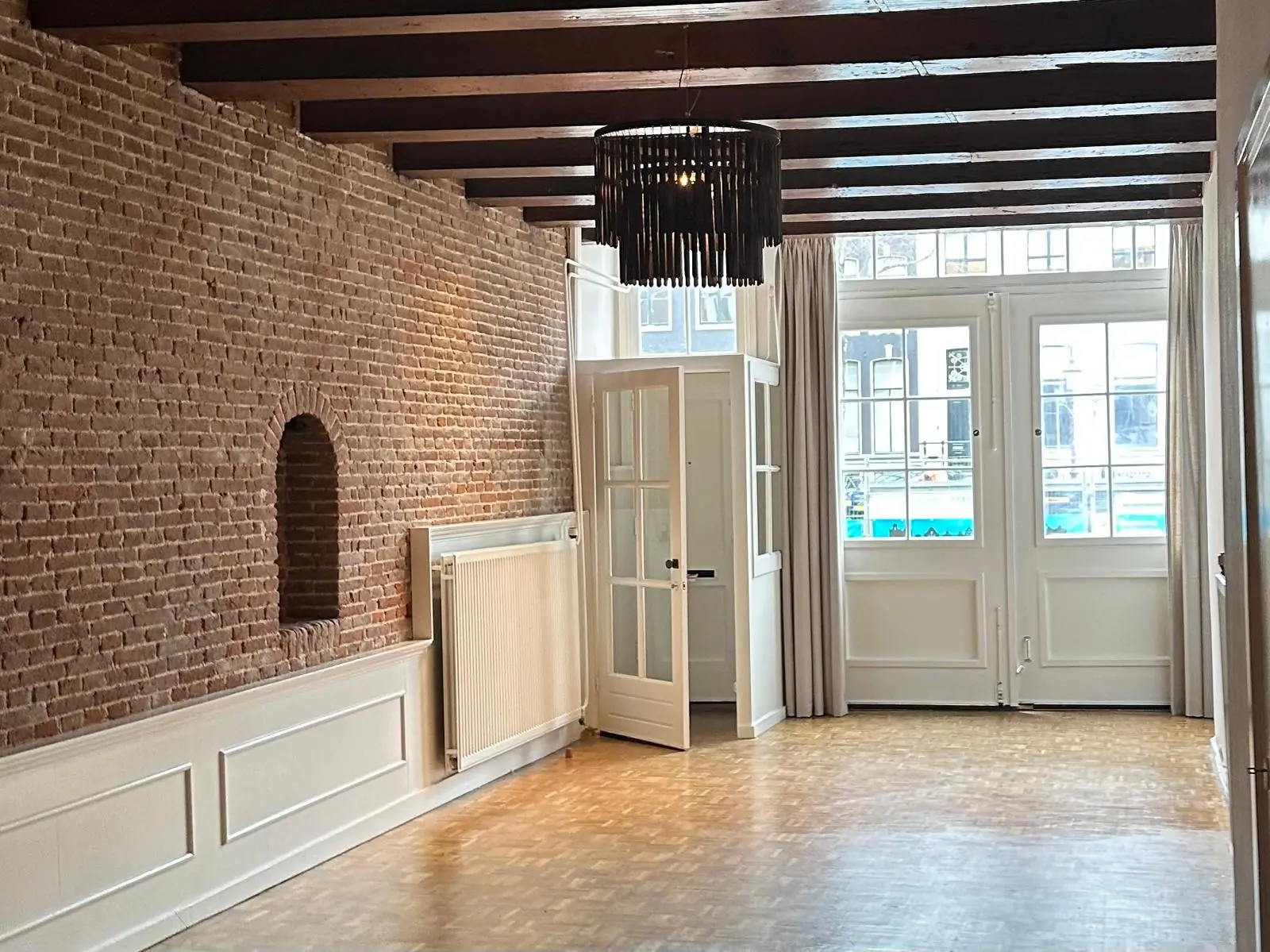 Lichte woonkamer aan de Herengracht met houten balkenplafond, bakstenen muur en grote ramen met uitzicht op de gracht.