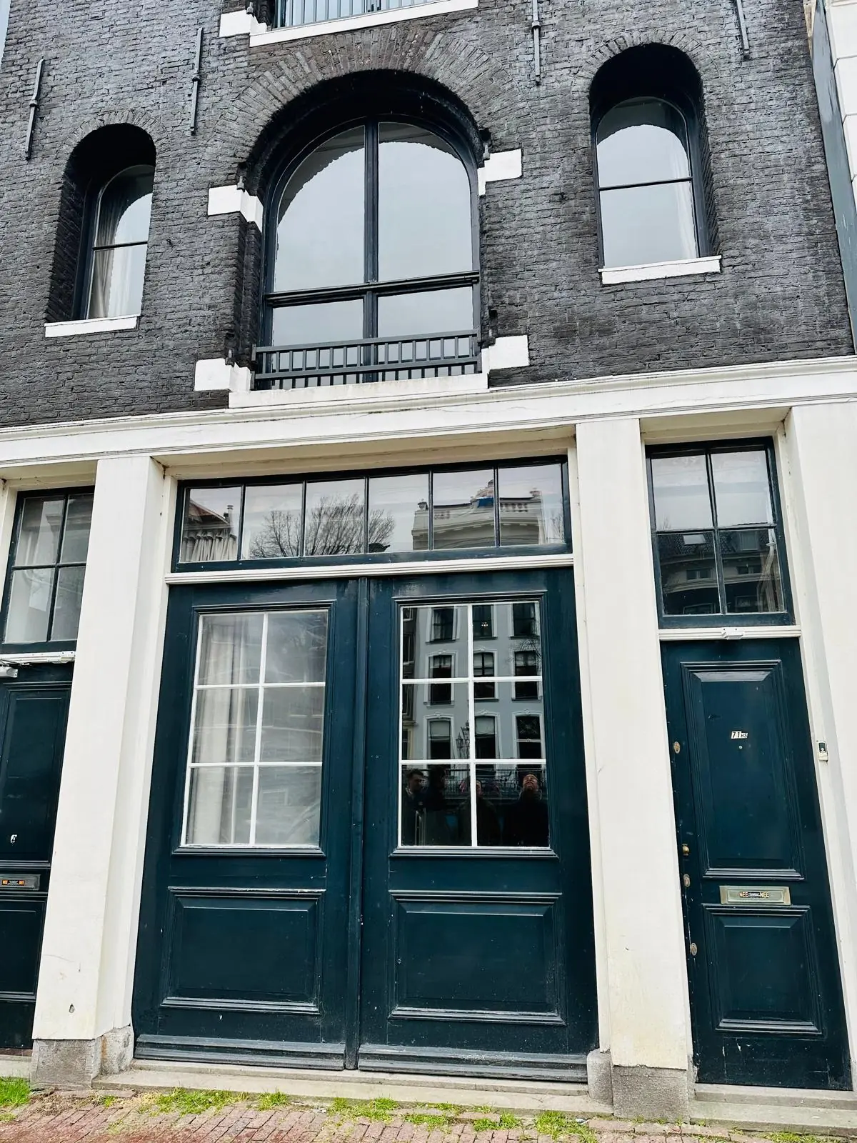 Voorgevel van een historisch pand aan de Herengracht met zwarte deuren en ramen met witte kozijnen.
