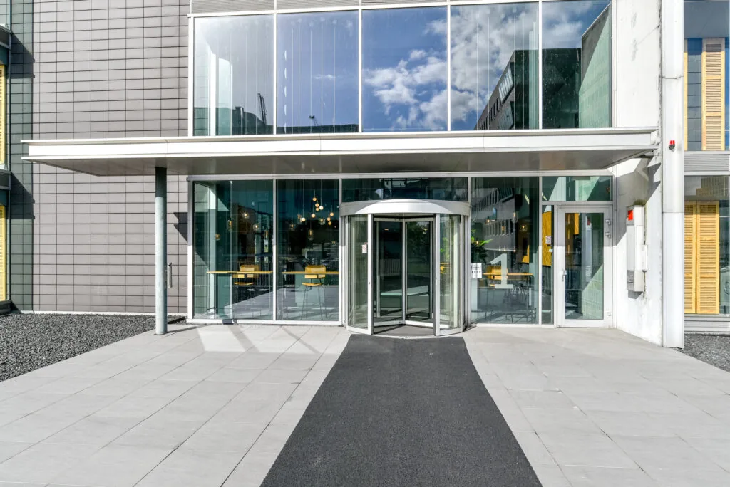 Hoofdingang van een modern kantoorgebouw aan de Paasheuvelweg met een glazen gevel en draaideur.