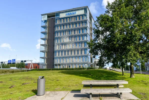 Modern kantoorgebouw aan de Paasheuvelweg met glazen gevel, zichtbaar vanaf een groen park met picknicktafel.