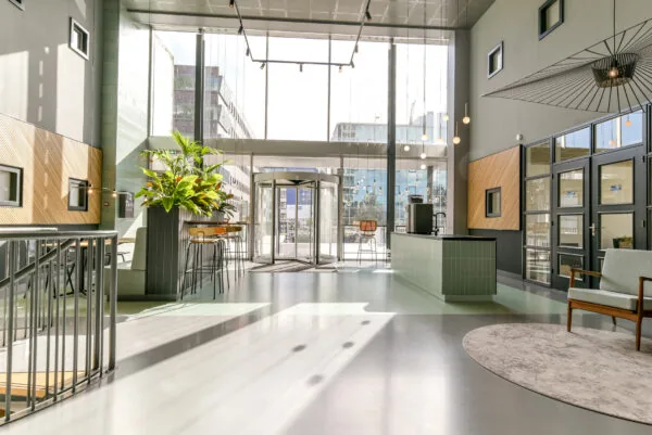 Moderne, lichtovergoten entreehal van een kantoorgebouw aan de Paasheuvelweg met zithoek, receptionistebalie en draaiende ingang.