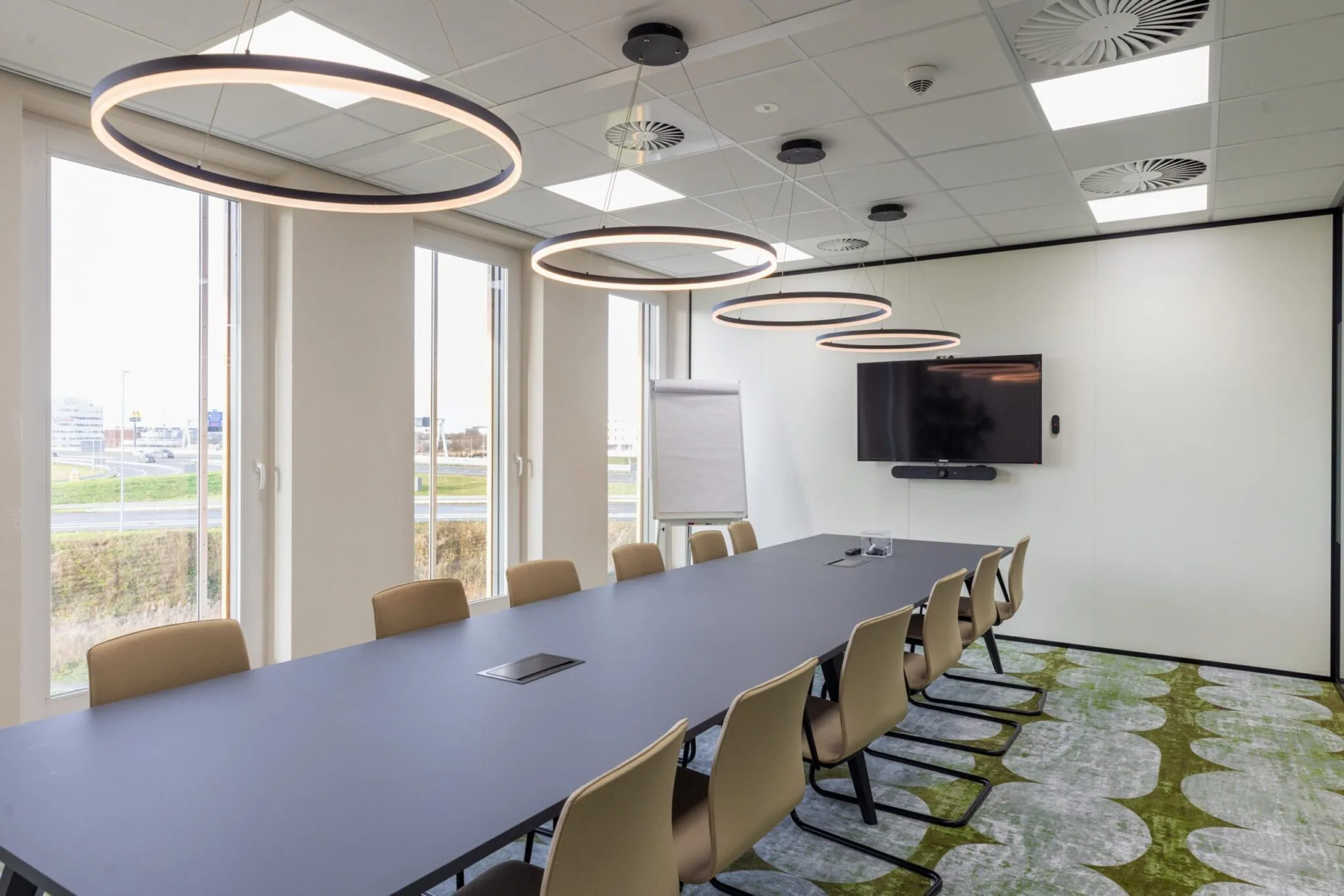 Moderne vergaderruimte aan de Paasheuvelweg met lange tafel, designverlichting, flatscreen en uitzicht op buiten.