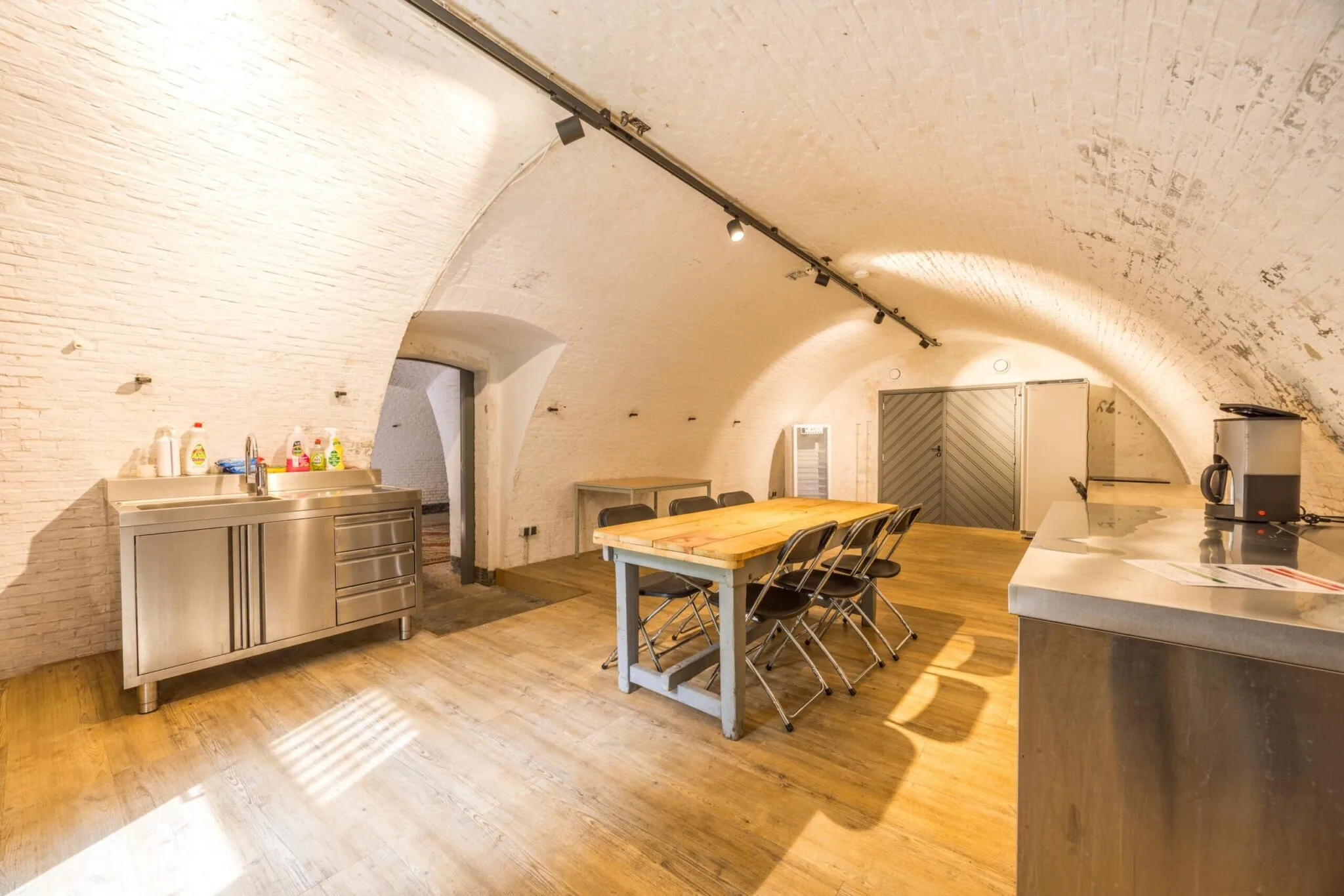 Ruimte met gewelfd plafond, houten vloer, lange tafel met stoelen en een roestvrijstalen keukenblok aan de Vossegatsedijk.
