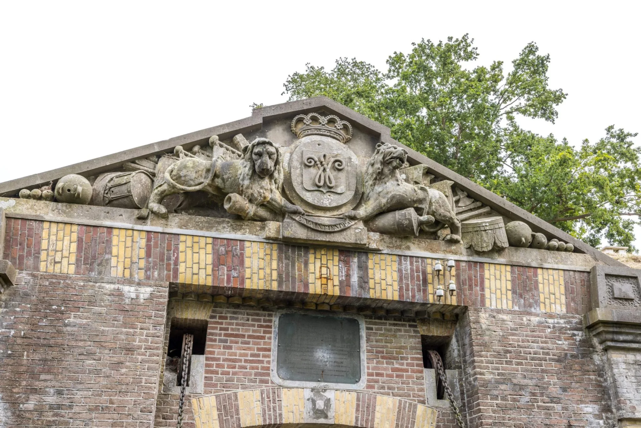 Gevel van een historisch fort aan de Vossegatsedijk met reliëf van twee leeuwen, een wapenschild en militaire ornamenten.