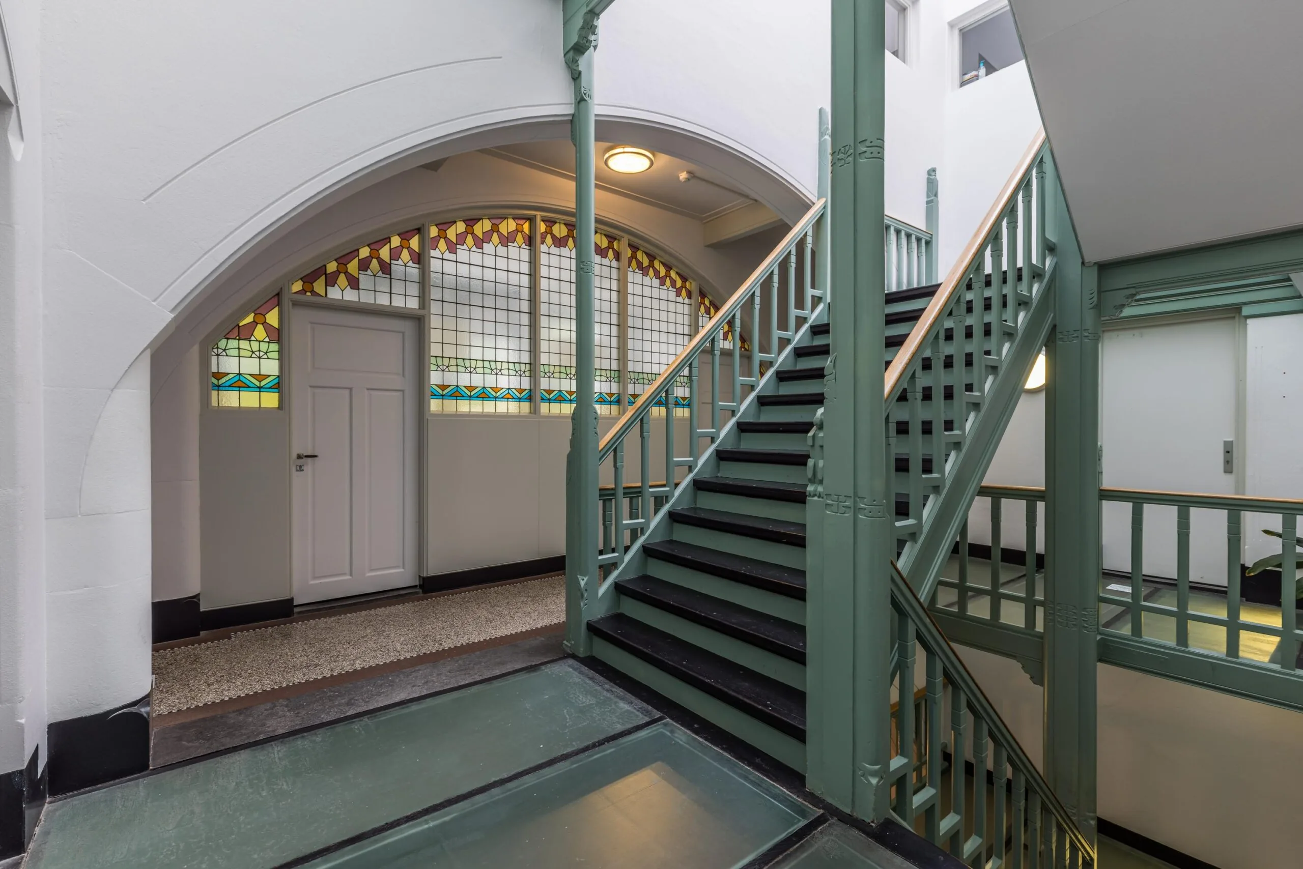 Trapportaal in een historisch pand aan de Driebergseweg met glas-in-loodramen en houten trap met groene balustrades.