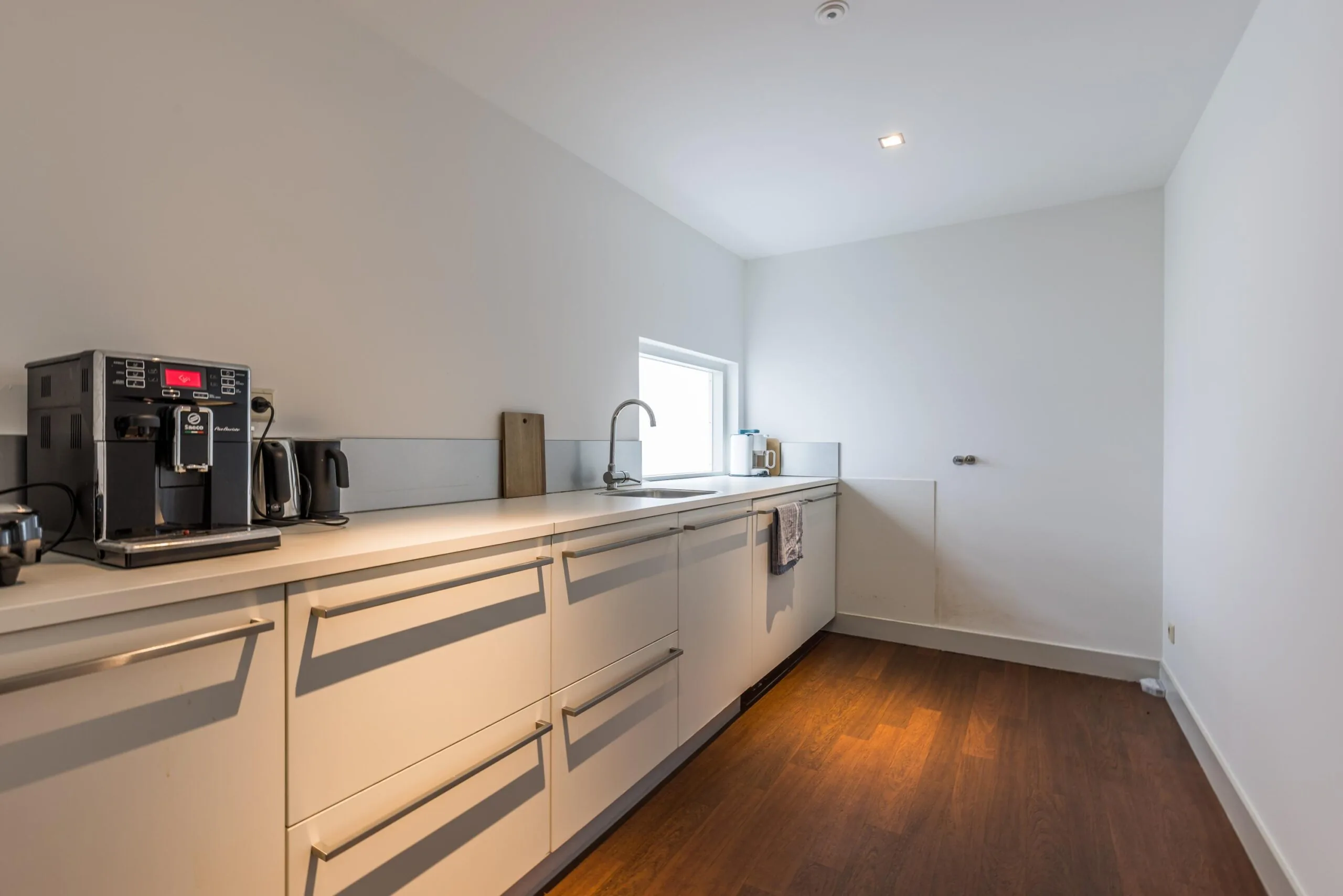 Moderne, minimalistische keuken aan de Driebergseweg met witte kasten, koffiemachine en houten vloer.