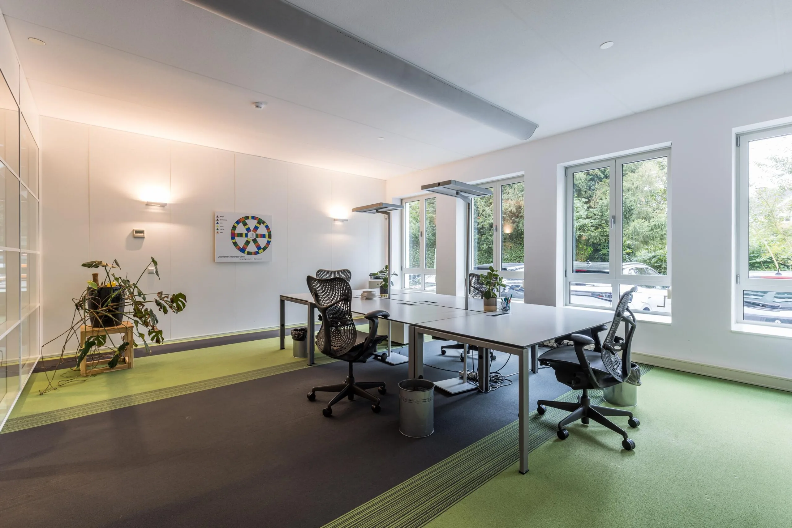 Modern kantoor met vier bureaus, ergonomische stoelen, veel natuurlijk licht en uitzicht op geparkeerde auto's aan de Driebergseweg.
