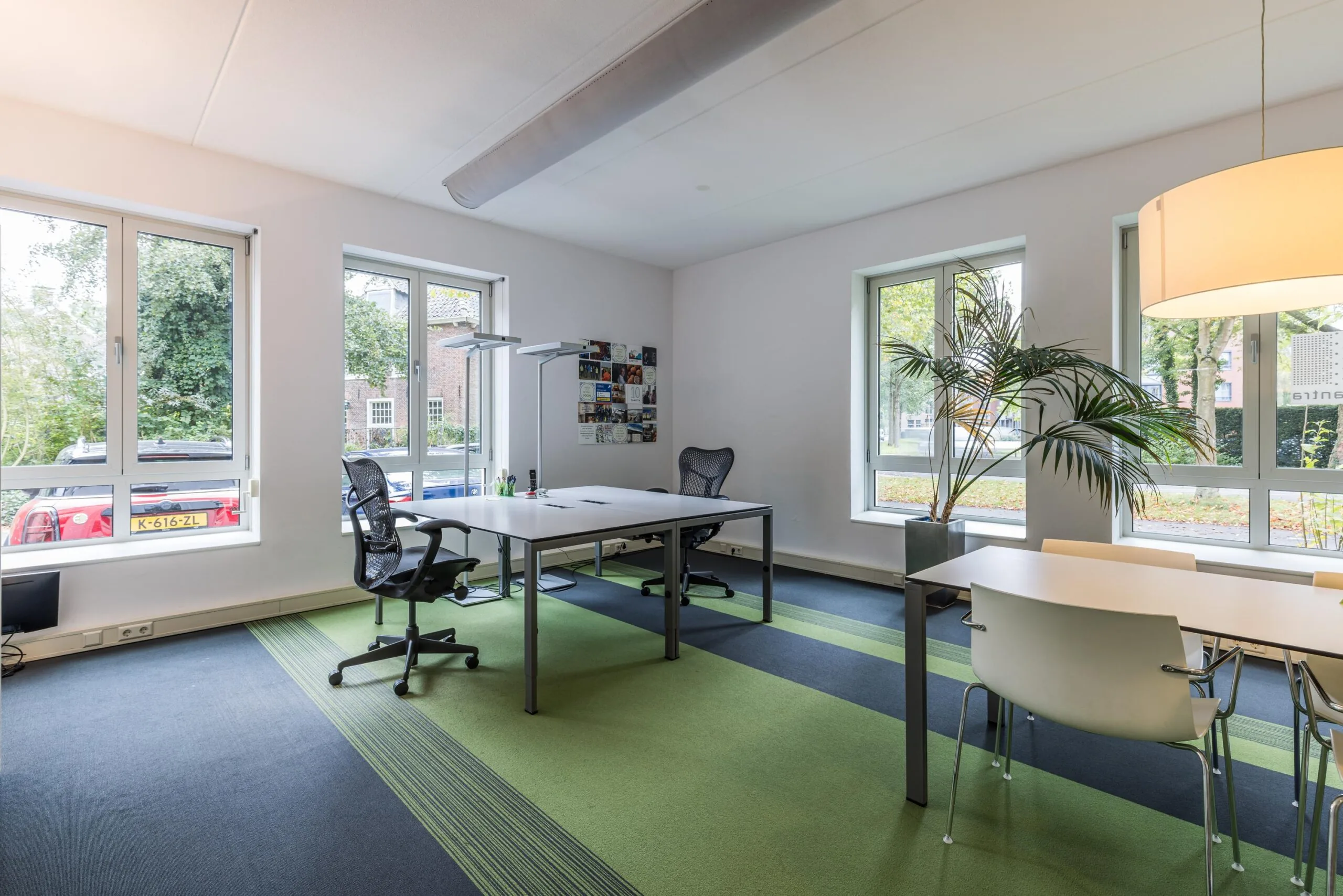 Modern ingericht kantoor aan de Driebergseweg met grote ramen, bureaus, bureaustoelen en een groene vloerbedekking.