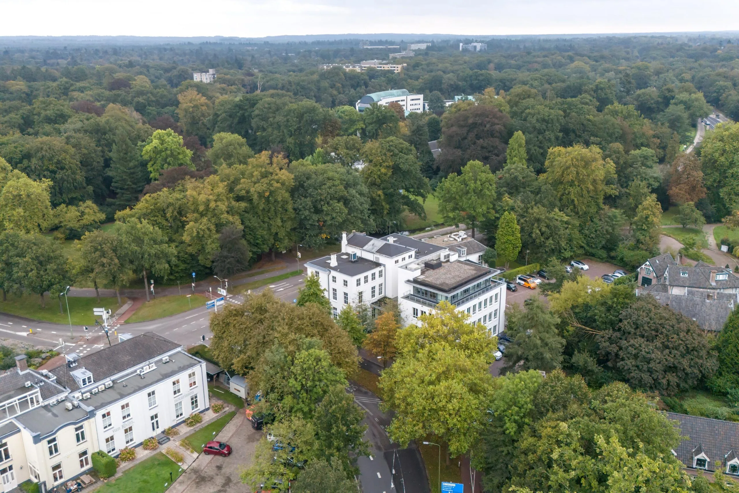 Luchtfoto van kantoren en omliggende bebouwing aan de Driebergseweg in een groene, bosrijke omgeving.