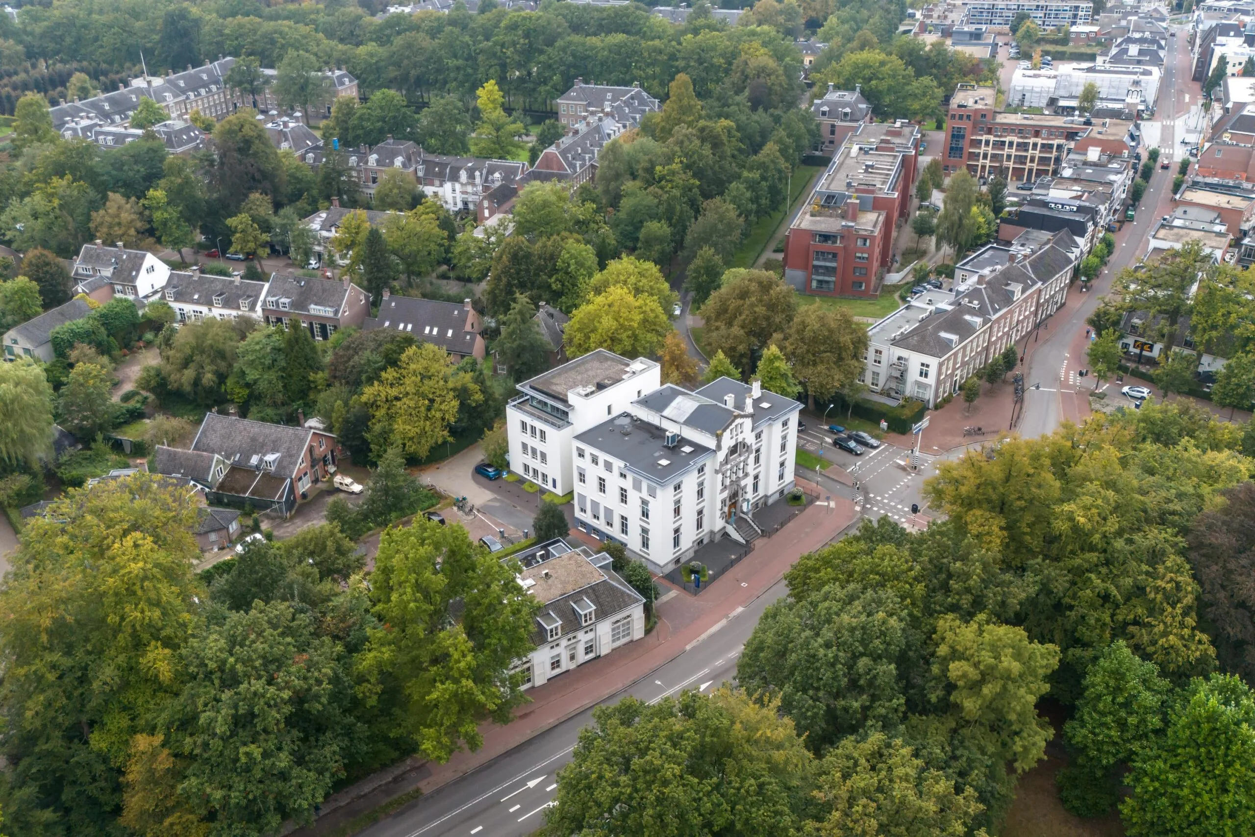 Luchtfoto van een wit herenpand aan de Driebergseweg in Zeist, omringd door woningen, bomen en stadsbebouwing.