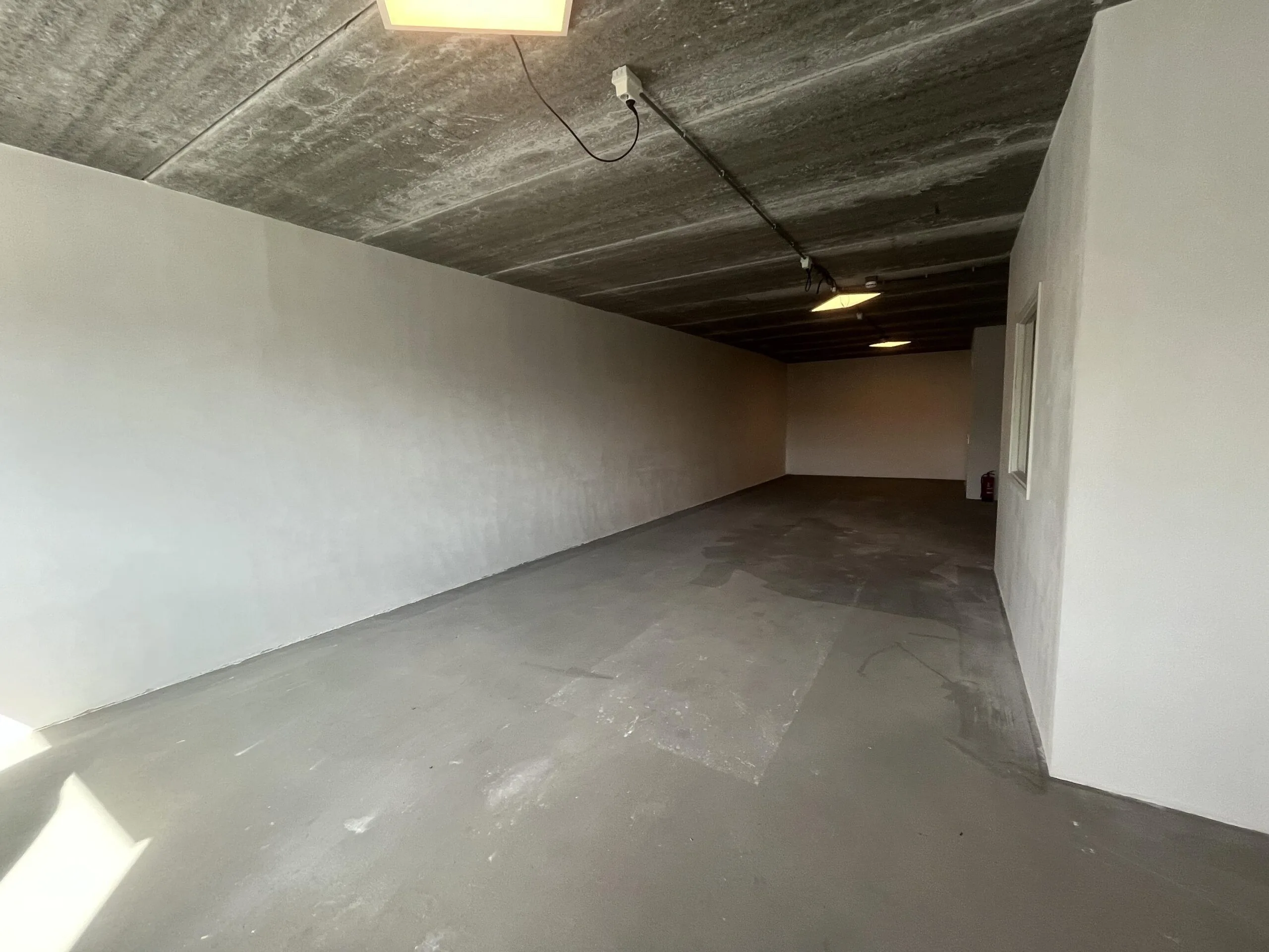 Een lege, eenvoudige ruimte met betonnen vloer en plafond, verlicht door enkele lampen.
