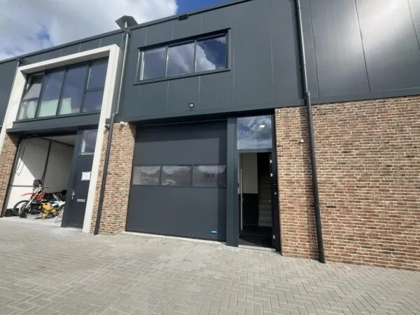 Een modern bedrijfsgebouw met een bakstenen gevel en een gesloten garagedeur, naast een open ruimte met een motorfiets erin.